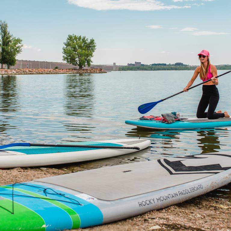 A young woman approaches the sandy beach at Cherry Creek State Park with her paddleboard